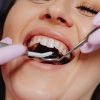 Smiling woman at dentist with tools for dental exam, highlighting dental care.