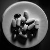 Artistic grayscale image of various pills on a saucer in top view.