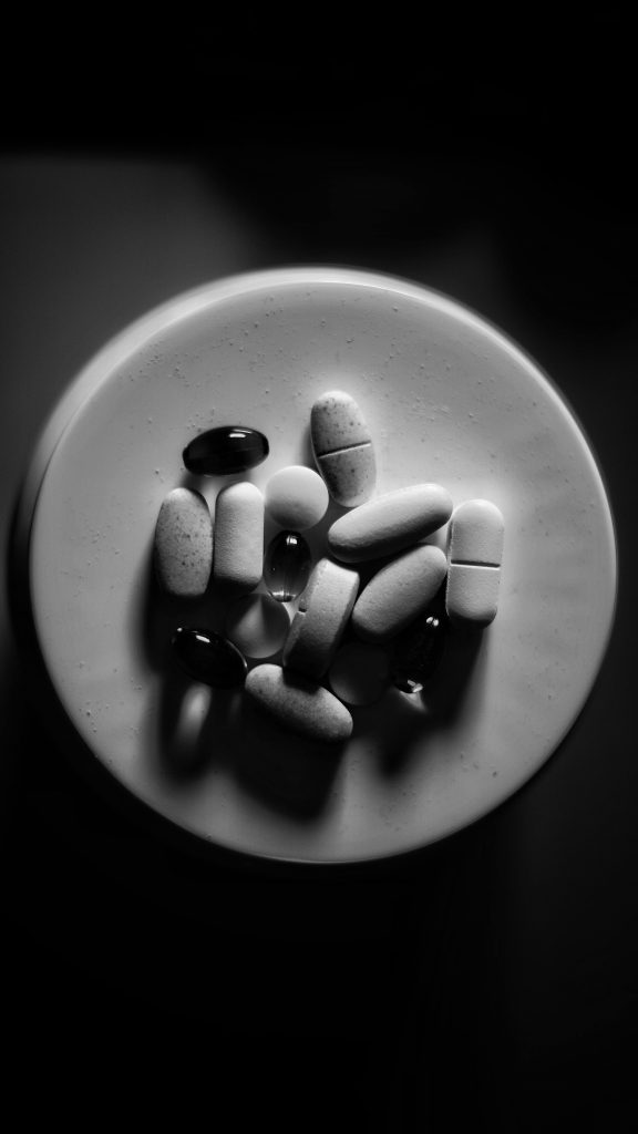 Artistic grayscale image of various pills on a saucer in top view.