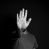 A person in the shadows raises a hand as a stop gesture in black and white.
