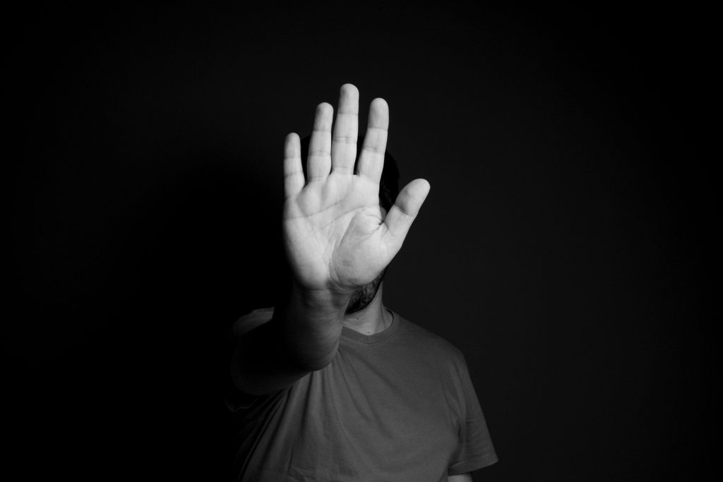 A person in the shadows raises a hand as a stop gesture in black and white.